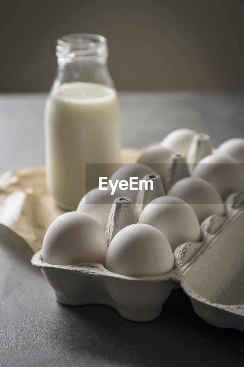 Close-up of eggs in carton with milk bottle on table