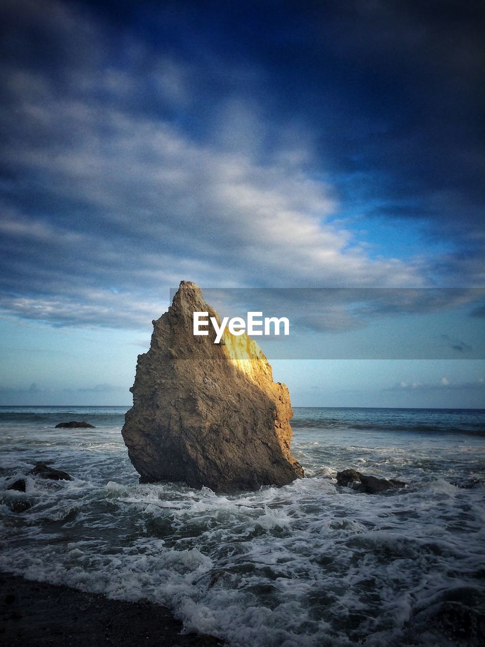 View of cliff in sea against cloudy sky