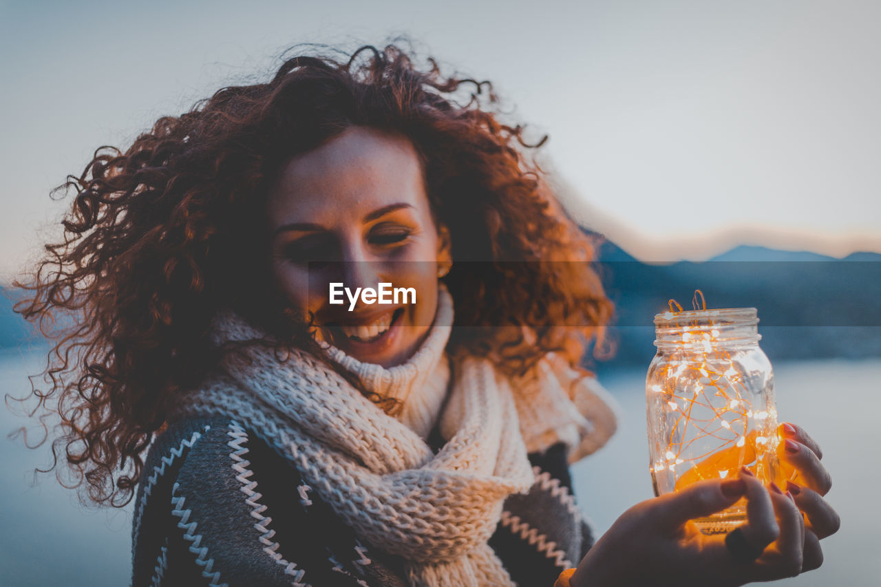 Smiling woman holding illuminated lights against sky