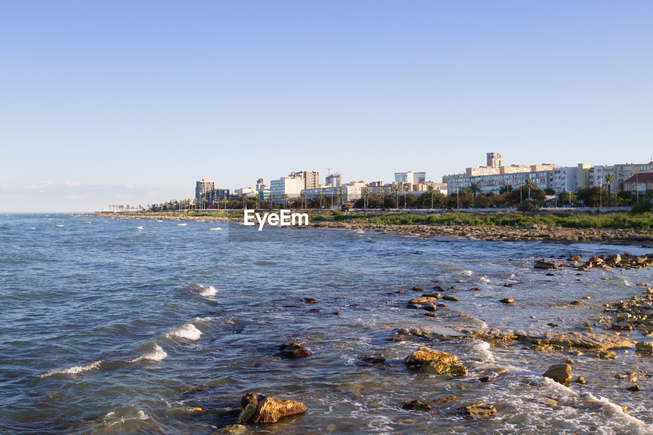 shore, water, architecture, city, coast, sea, building exterior, built structure, sky, body of water, building, beach, horizon, nature, clear sky, ocean, travel destinations, land, cityscape, bay, urban skyline, no people, travel, landscape, blue, outdoors, office building exterior, residential district, day, skyscraper, tourism, sunny, environment, wave, city life, coastline