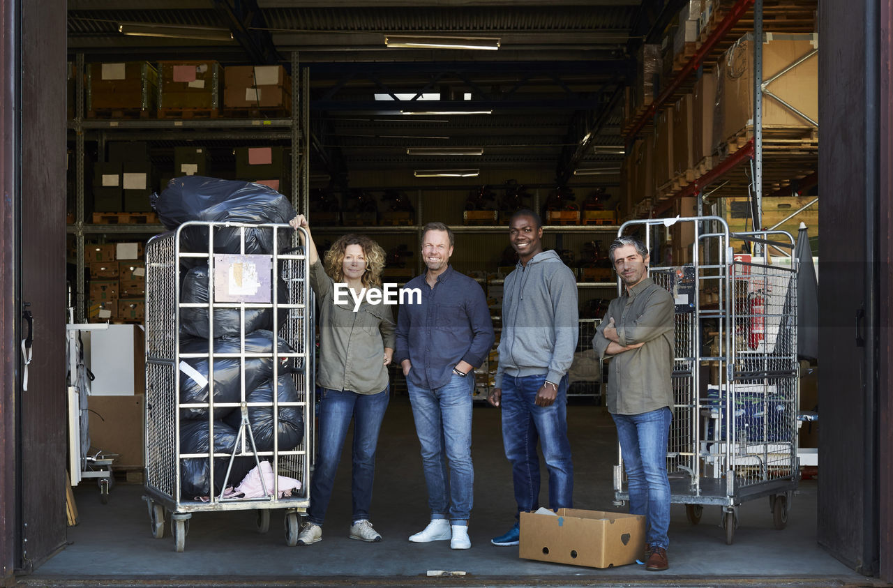 Portrait of smiling coworkers standing amidst carts at warehouse doorway