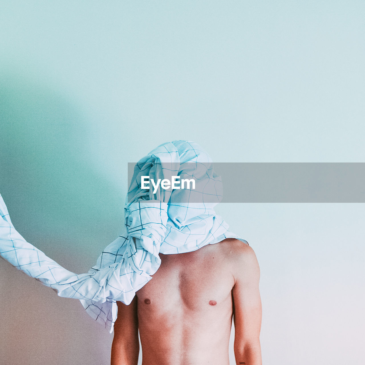 Shirtless man face covered with fabric against white wall
