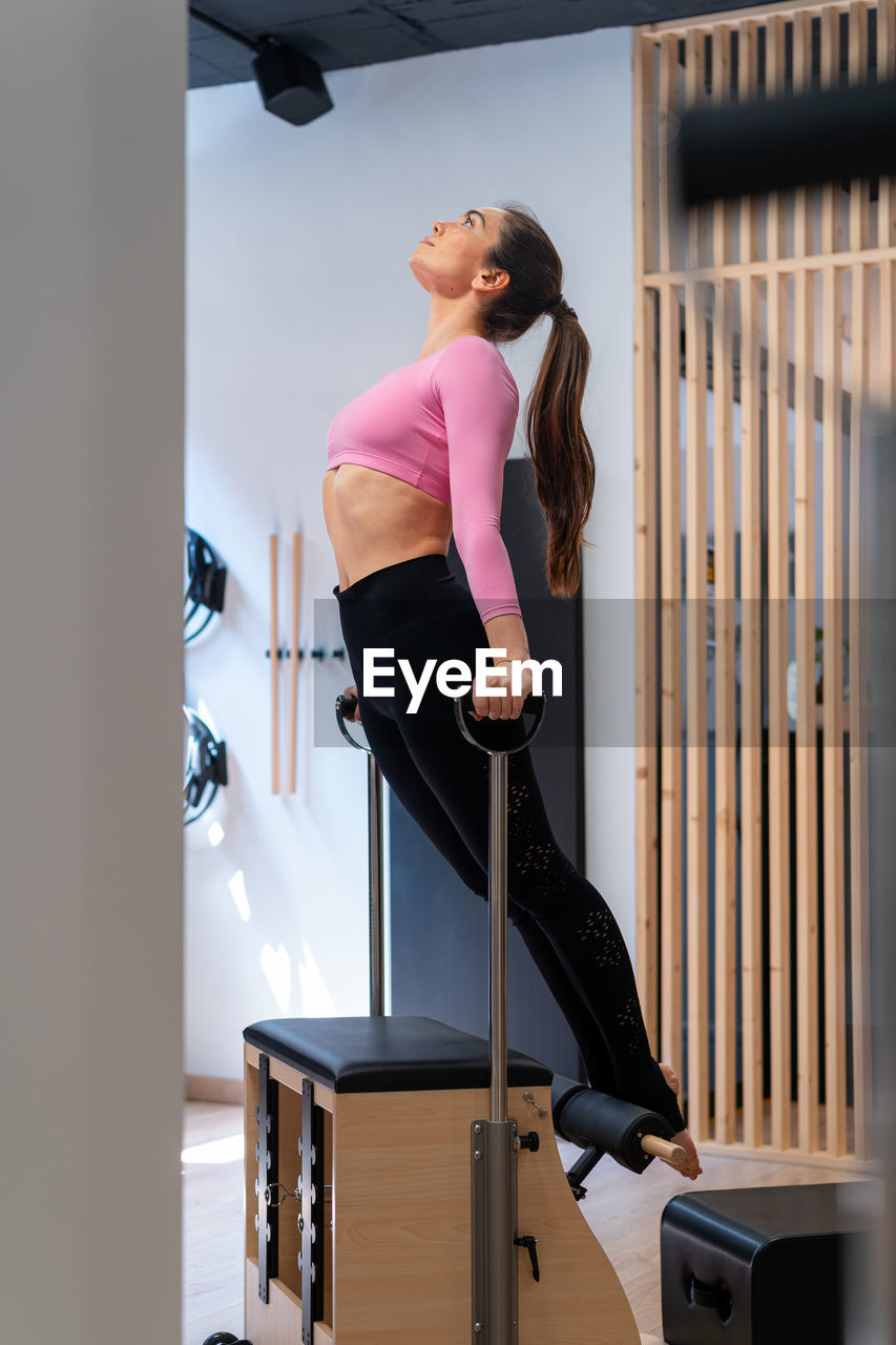 Side view of fit sportswoman doing balance exercise on pilates chair during workout in gym