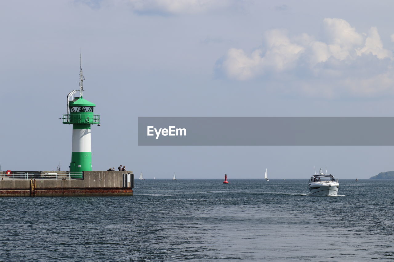 Lighthouse on sea by building against sky