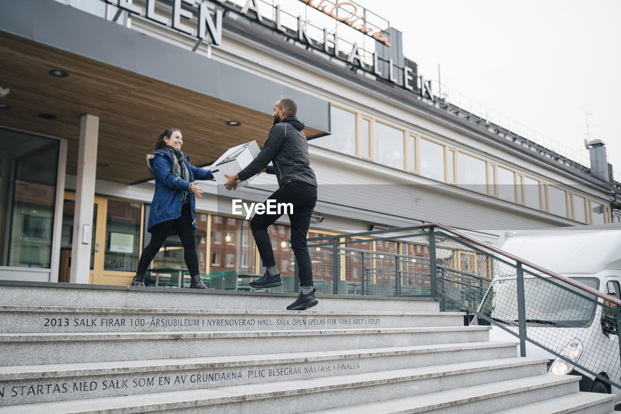 Low angle view of messenger delivering box to female customer in city