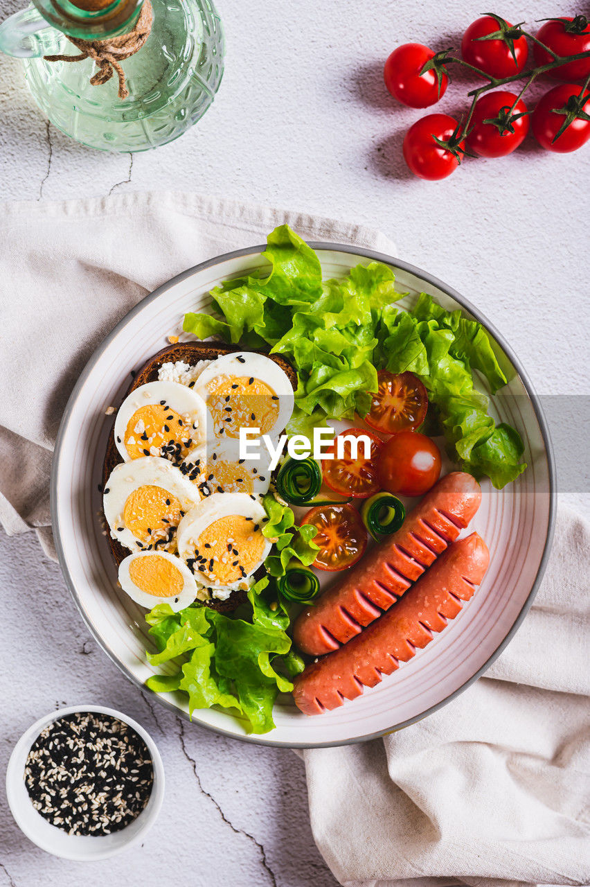 Plate with sausages, egg sandwich, tomatoes and lettuce leaves on the table top and vertical view