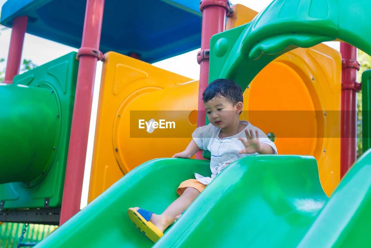 Full length of cute boy sitting on slide at playground