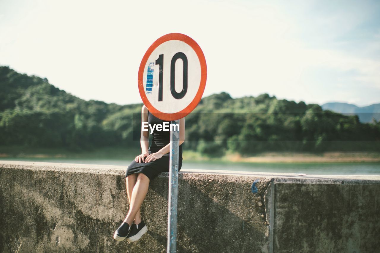 Woman sitting on retaining wall behind speed limit signboard