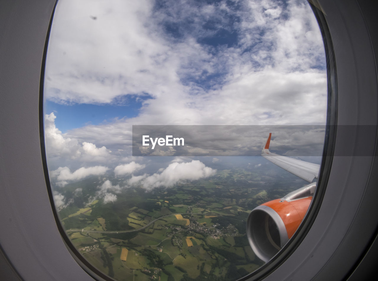 Aircraft wing and jet engine seen though glass window against cloudy sky