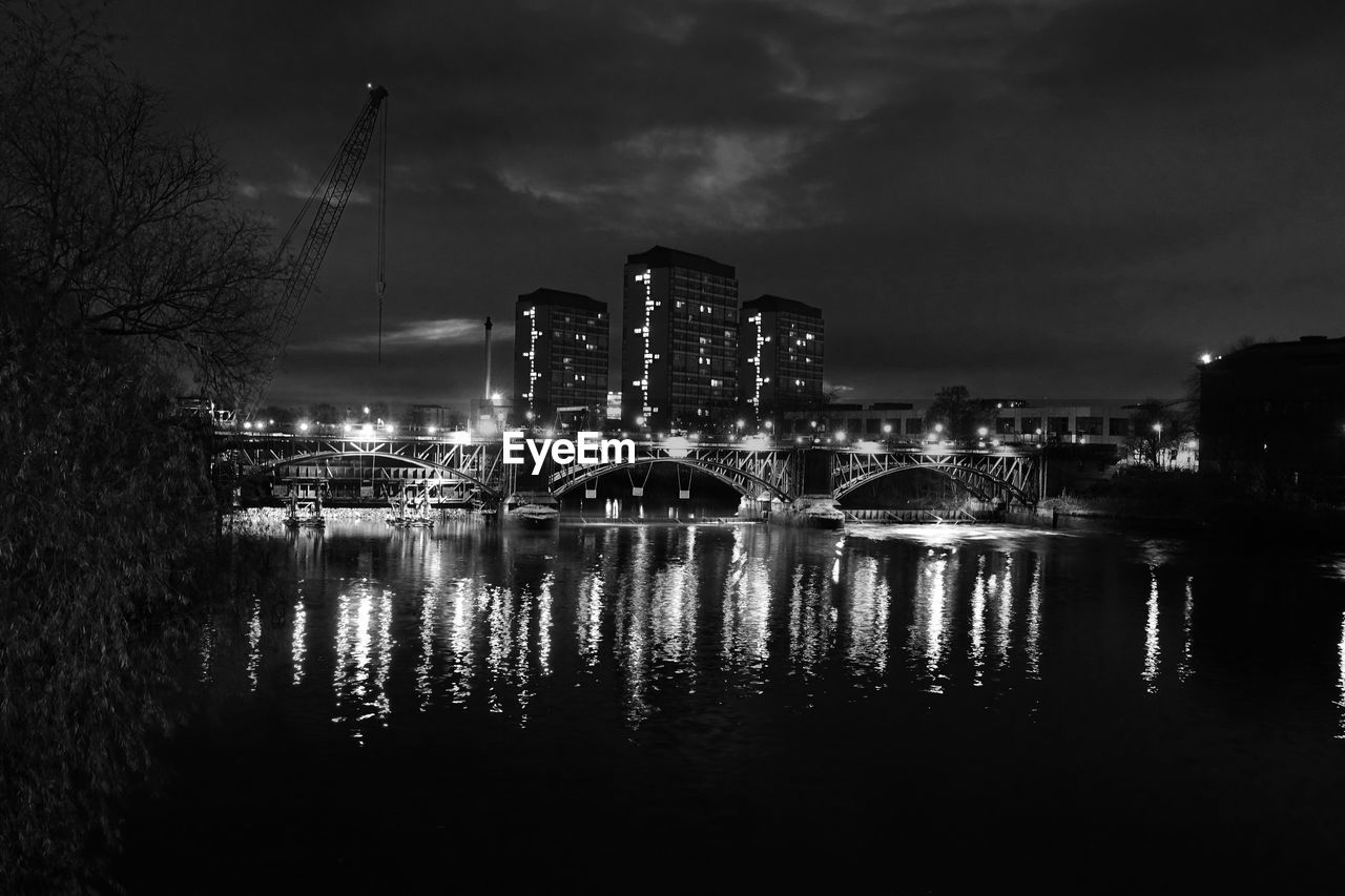 Illuminated buildings by river against sky in city at night