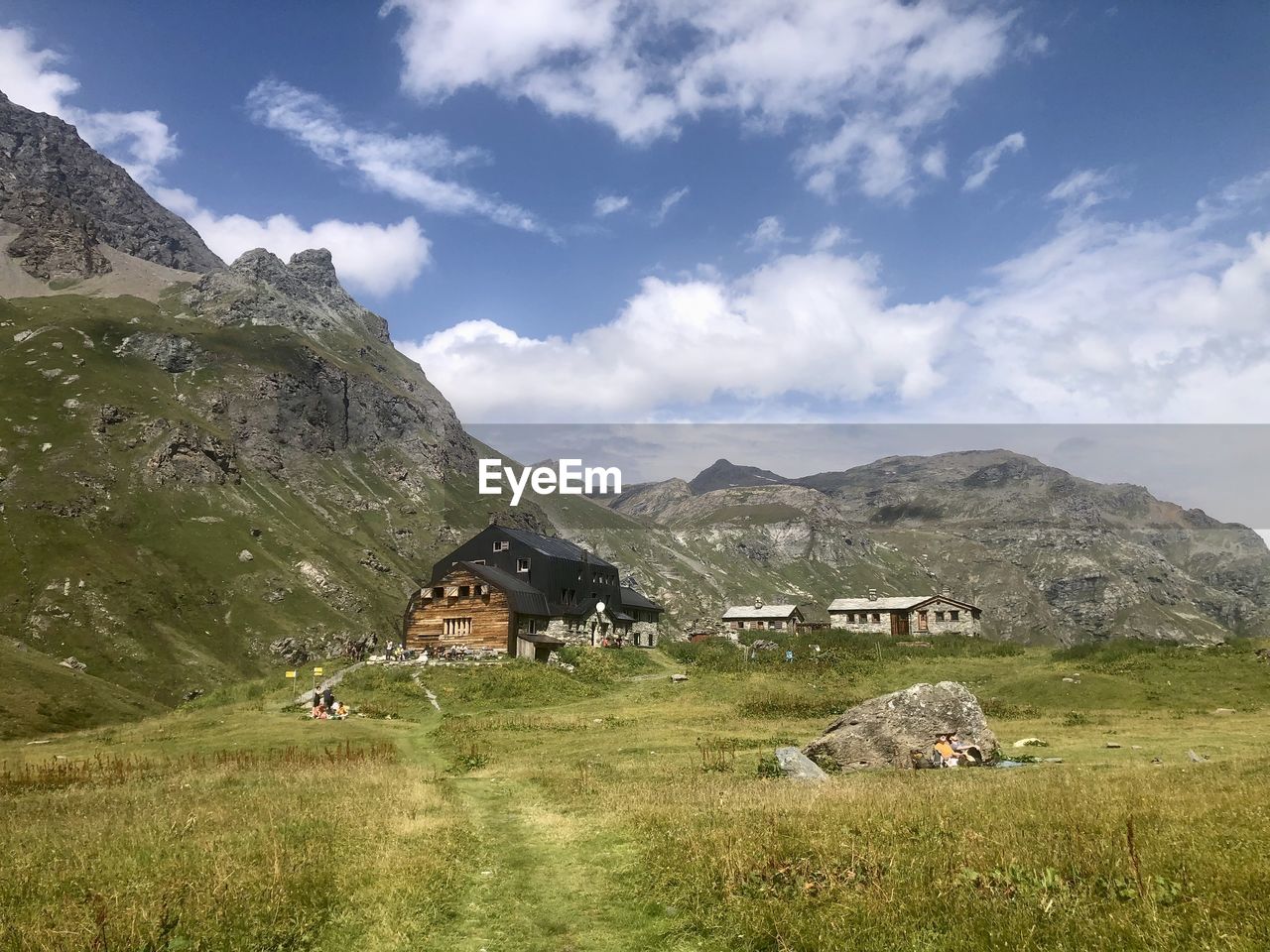 mountain, mountain range, landscape, environment, sky, grass, scenics - nature, nature, land, plant, meadow, cloud, beauty in nature, highland, architecture, building, plateau, house, built structure, travel, wilderness, field, valley, travel destinations, grassland, rural scene, building exterior, no people, plain, pasture, tranquility, outdoors, green, village, tourism, domestic animals, non-urban scene, hut, livestock, rural area, tranquil scene, residential district, day, ridge, activity, agriculture, tree, walking, mountain peak, idyllic, mammal, summer, social issues, lake