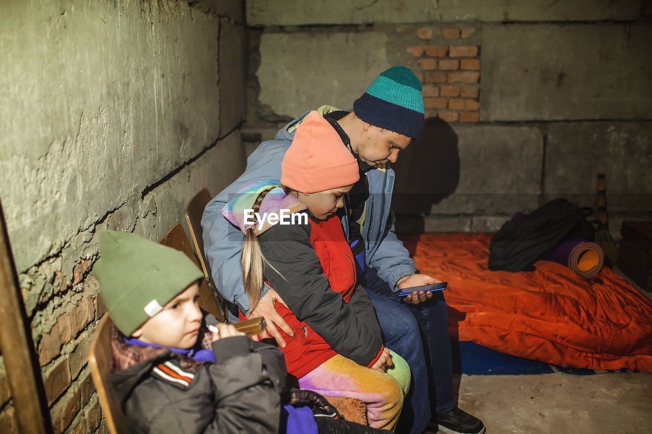Ukrainian father with kids sits in bomb shelter and reads latest braking news about russian invaders