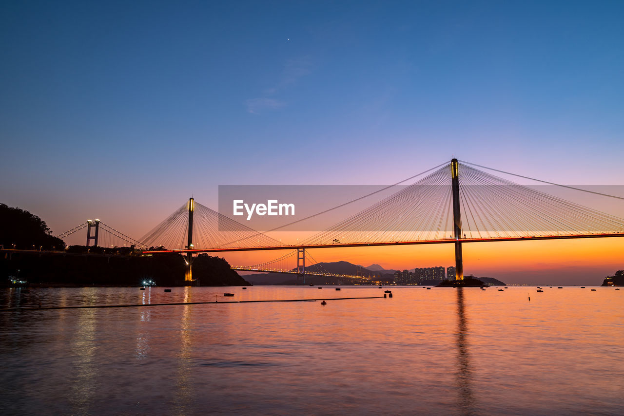 water, bridge, sky, architecture, transportation, suspension bridge, built structure, dusk, travel destinations, nature, reflection, sunset, evening, sea, city, horizon, travel, engineering, tourism, beauty in nature, night, scenics - nature, blue, landscape, bay, cable-stayed bridge, bay of water, twilight, cityscape, outdoors, tranquility, dramatic sky, illuminated, copy space, cloud, building exterior, urban skyline, long exposure, nautical vessel, mode of transportation, tranquil scene, environment, city life, red, business finance and industry, building