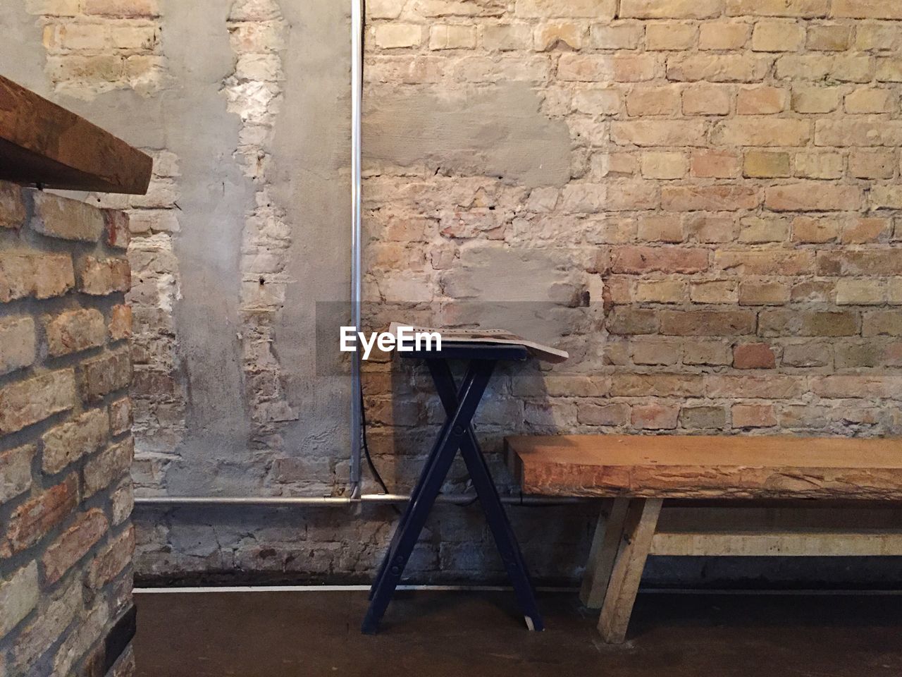 Empty wooden bench by old brick wall at cafe