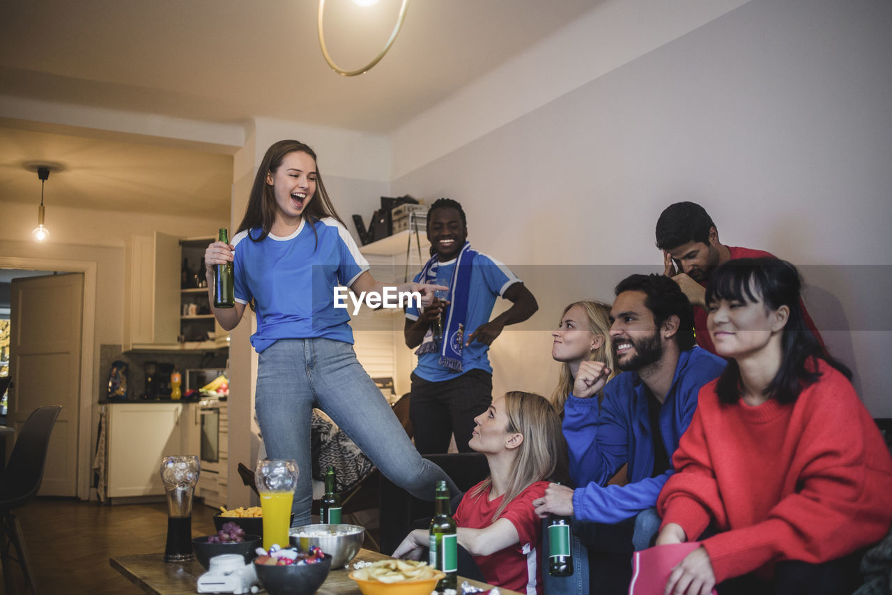 Smiling woman pointing at female while watching sport with friends at home