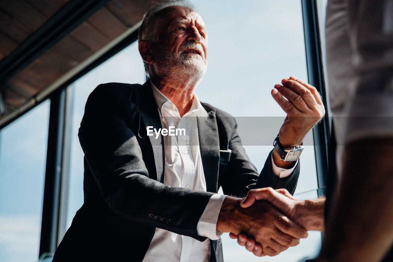 Low angle view of business person shaking hand while having discussion in office