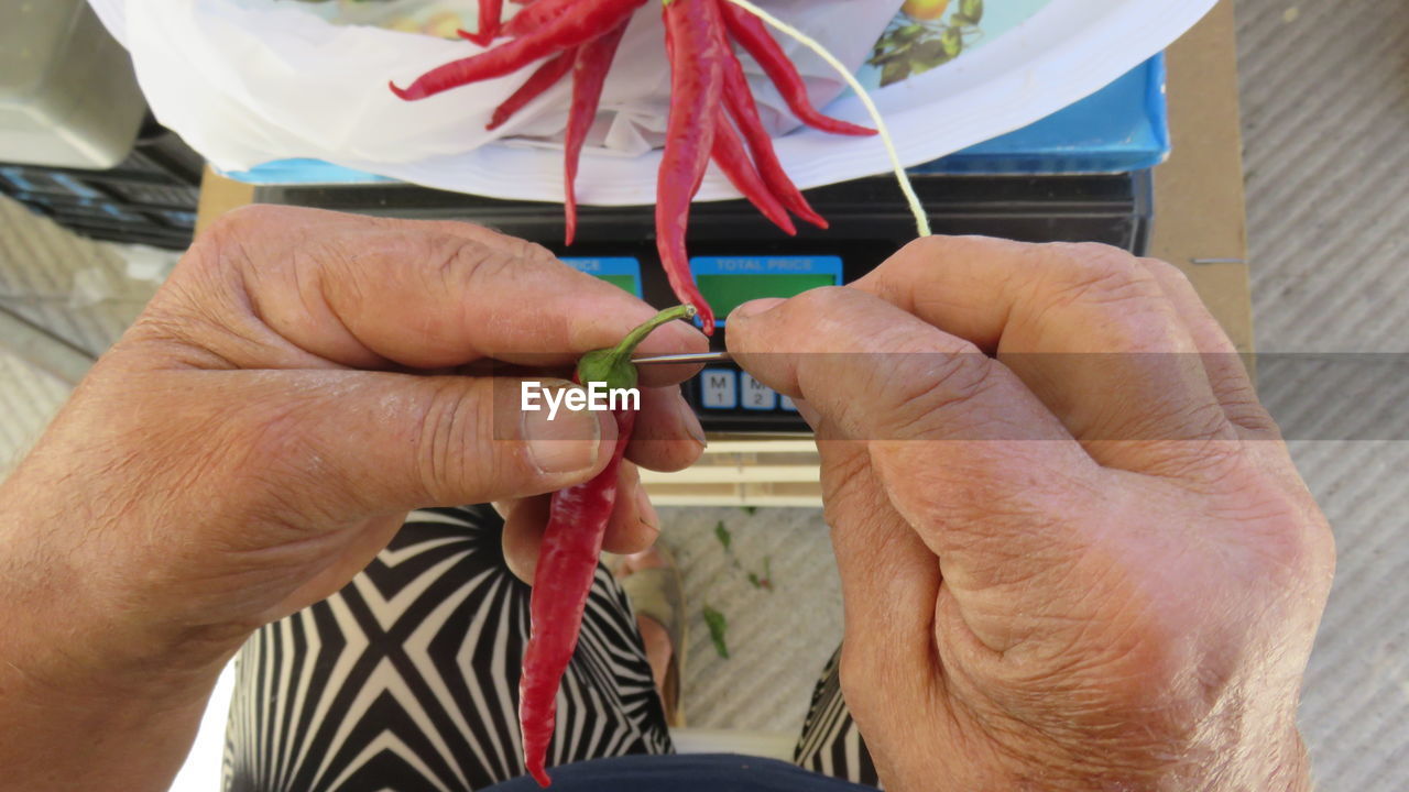 Low section of person stringing red chili peppers