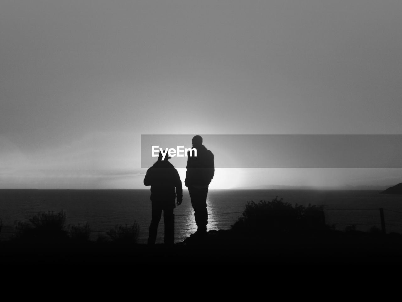 Silhouette friends standing on sea shore against sky