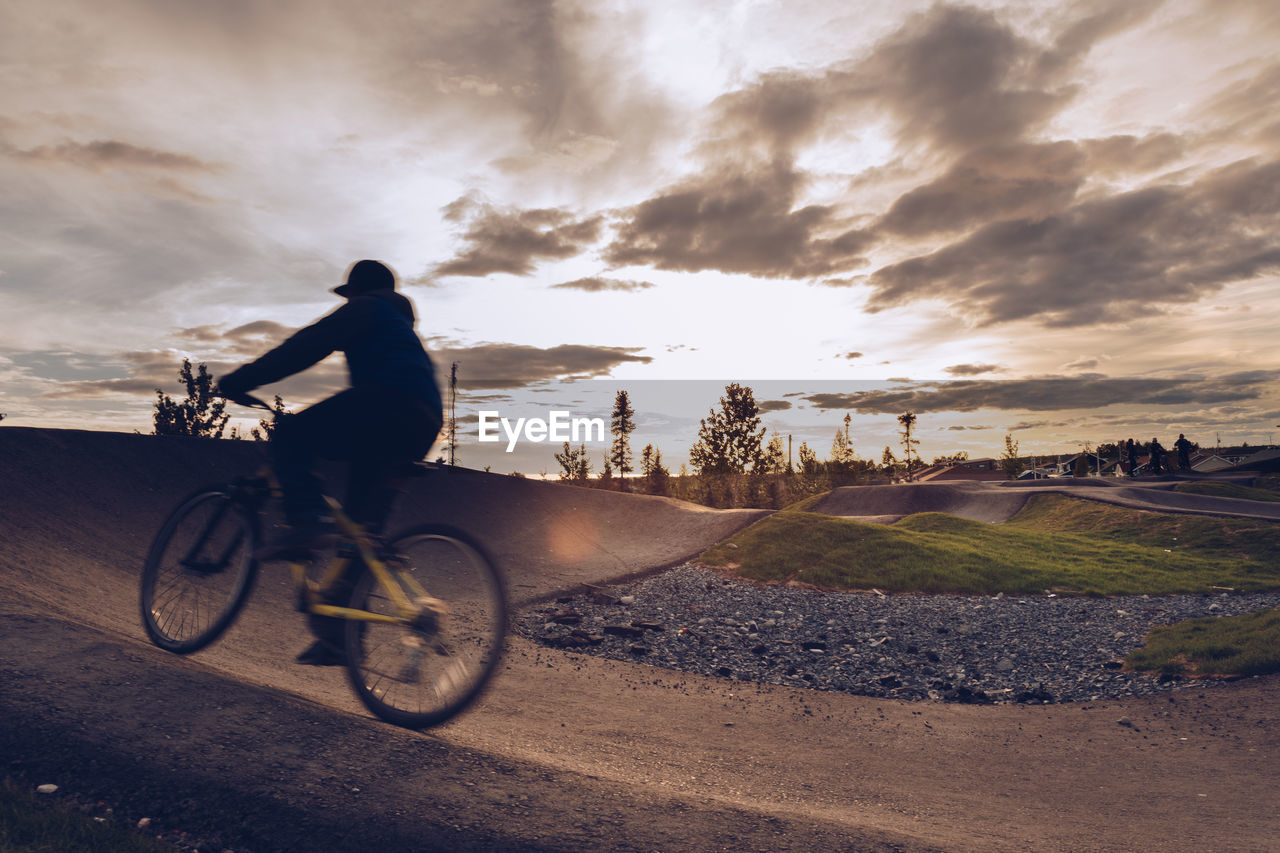 Man riding bicycle against sky during sunset