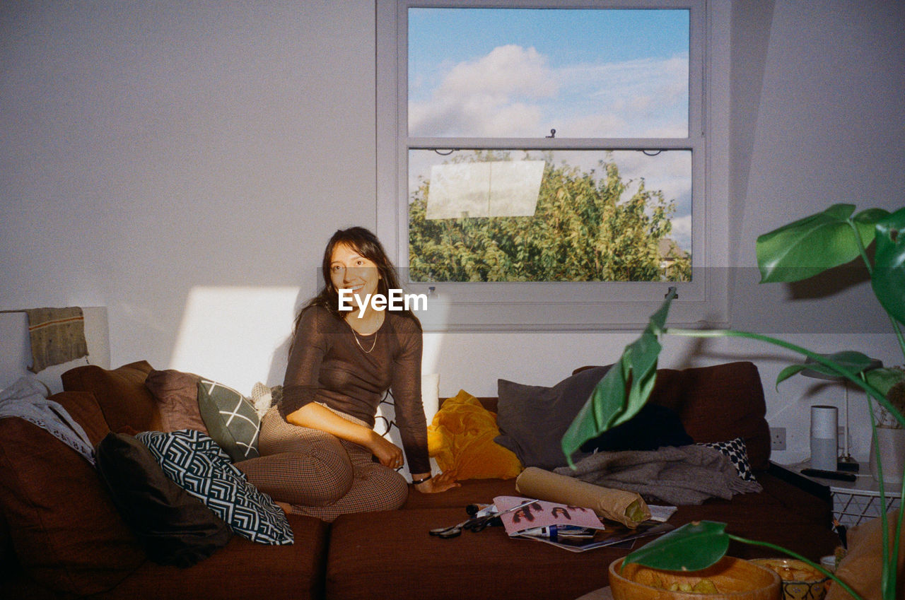 PORTRAIT OF YOUNG WOMAN SITTING ON SOFA AT HOME