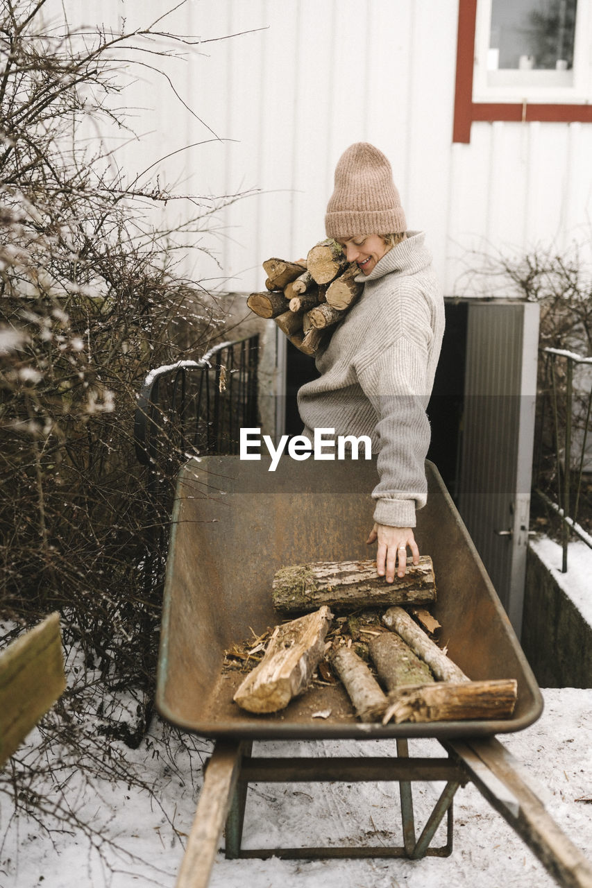 Woman collecting firewood from wheelbarrow during winter