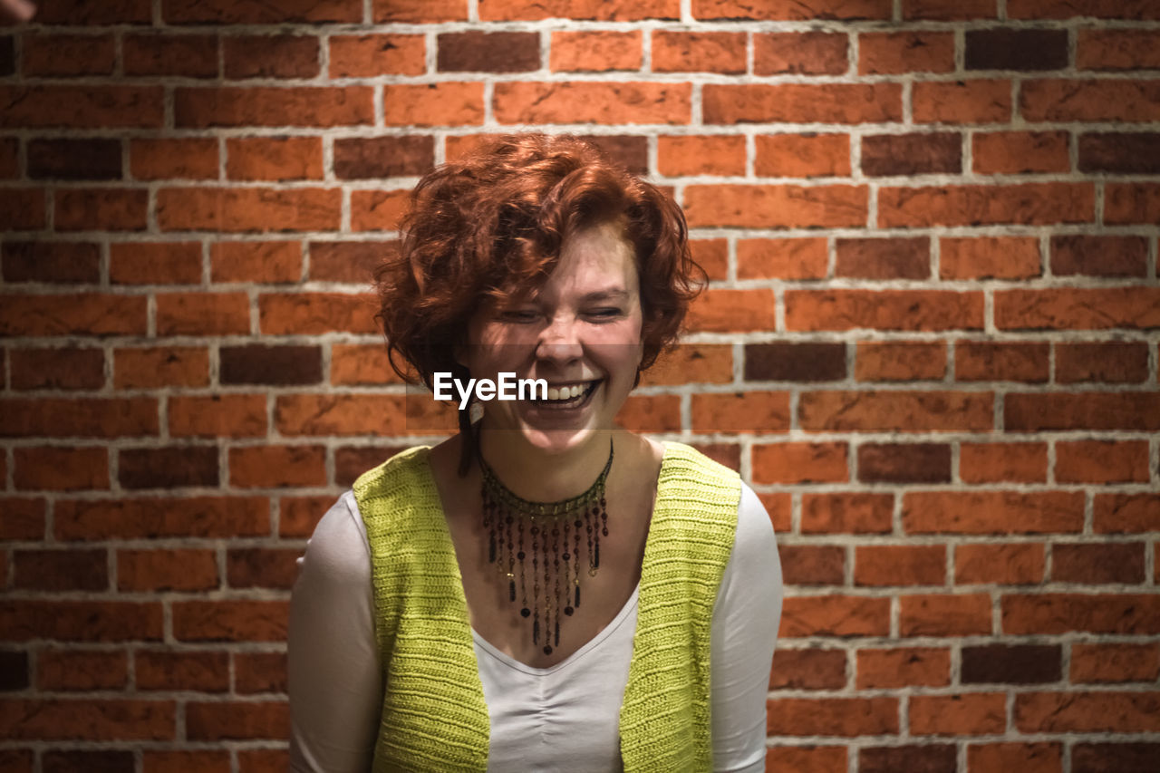 Cheerful young woman against brick wall