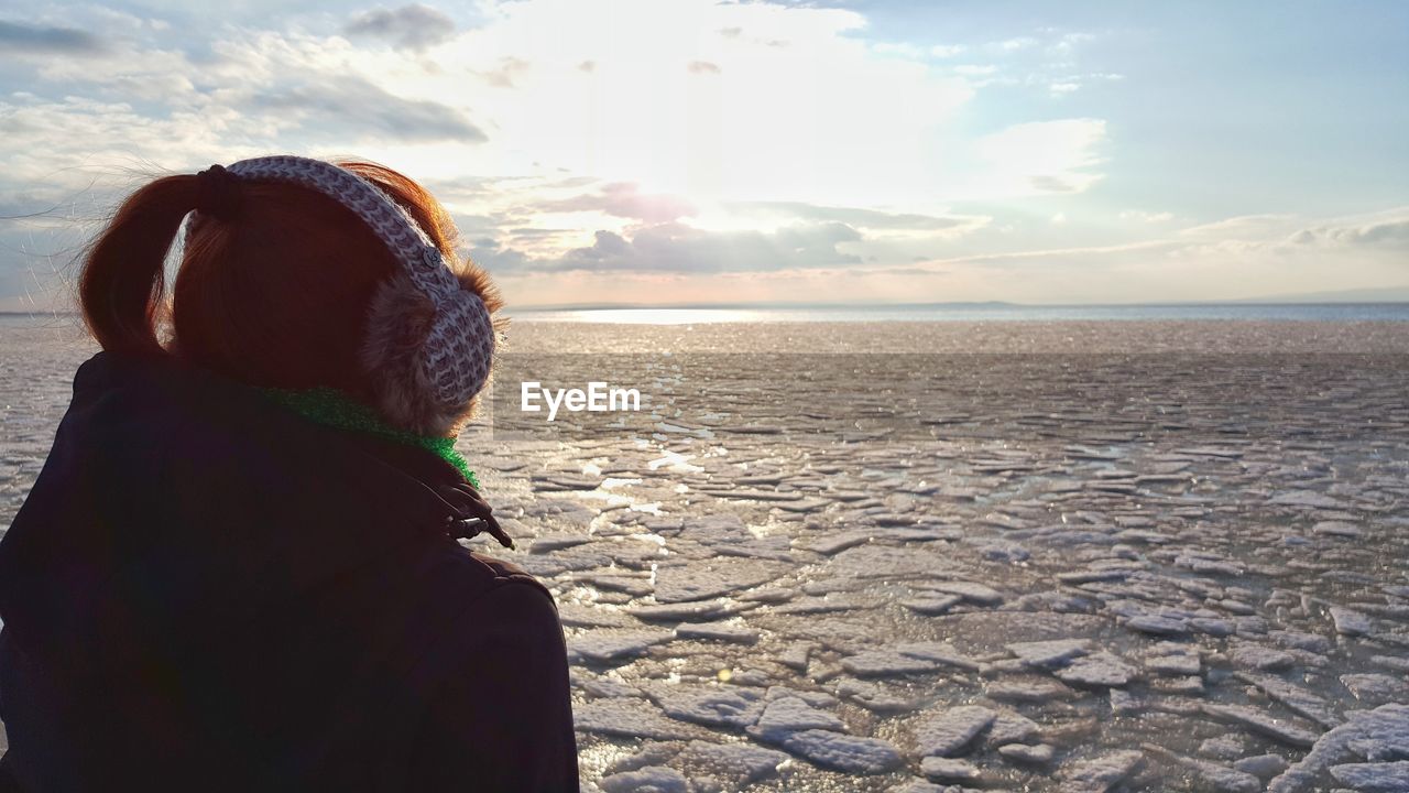 Close-up of woman wearing headphones at beach against sky during winter