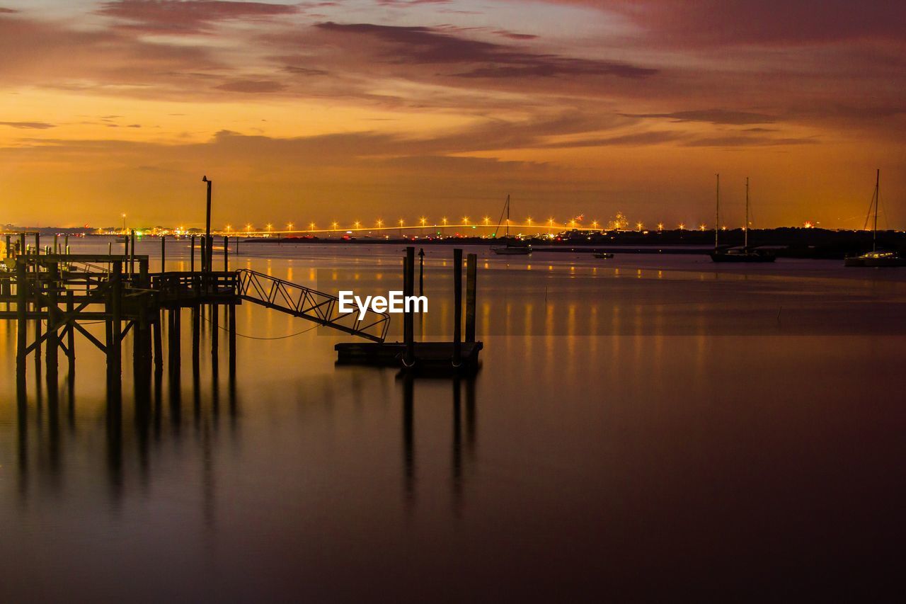 Pier over river against sky during sunset