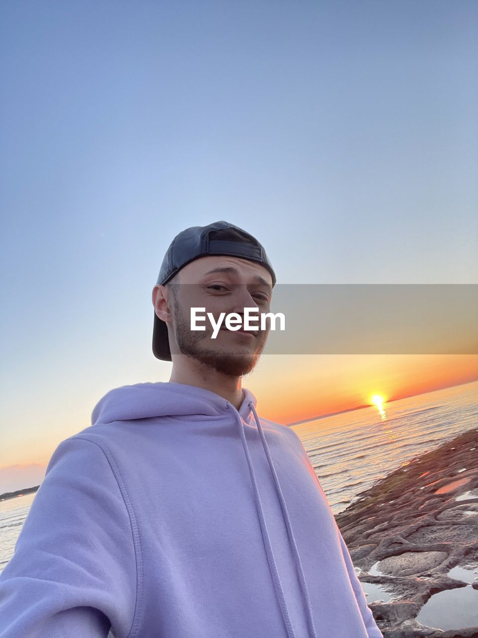 YOUNG MAN LOOKING AWAY AGAINST SKY DURING SUNSET