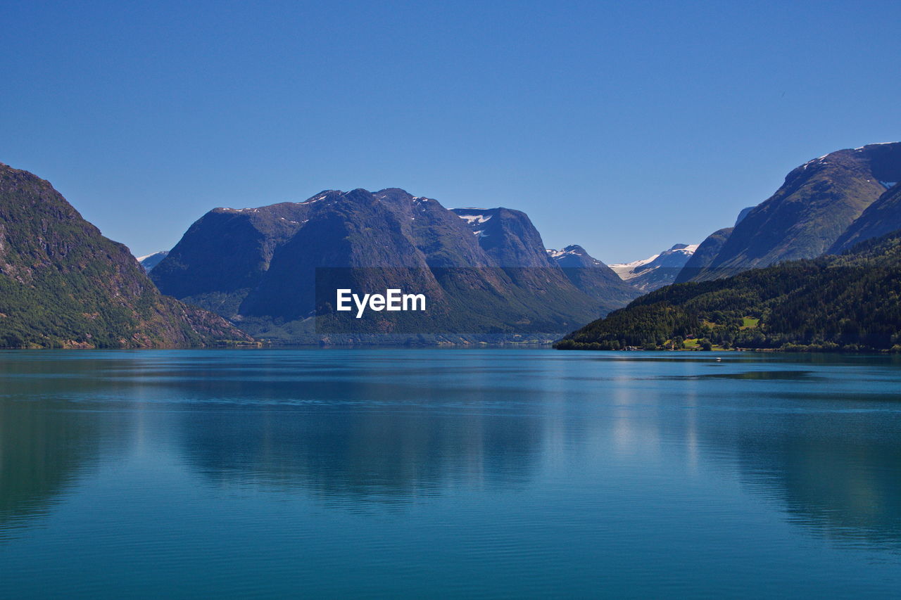 Scenic view of lake and mountains against clear blue sky