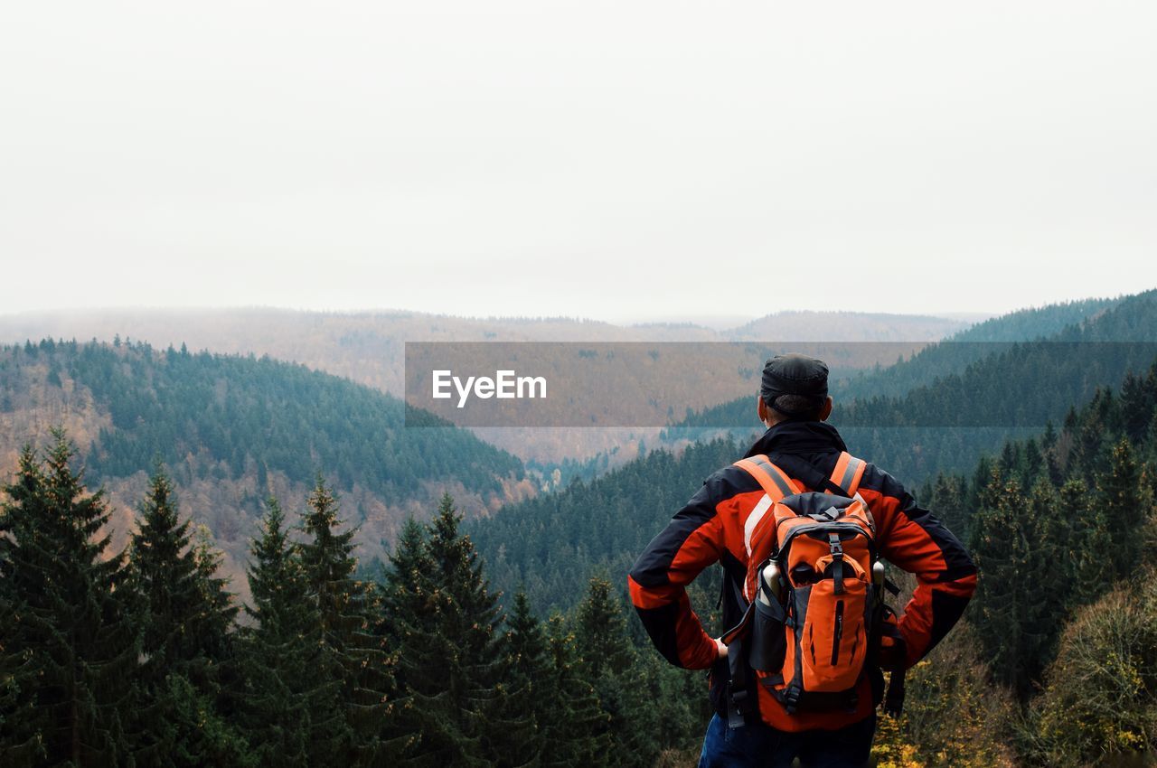 Rear view of man with backpack looking at mountains against sky