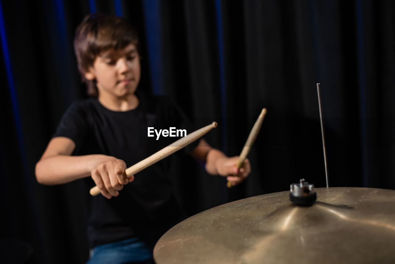 Boy playing drum against black background