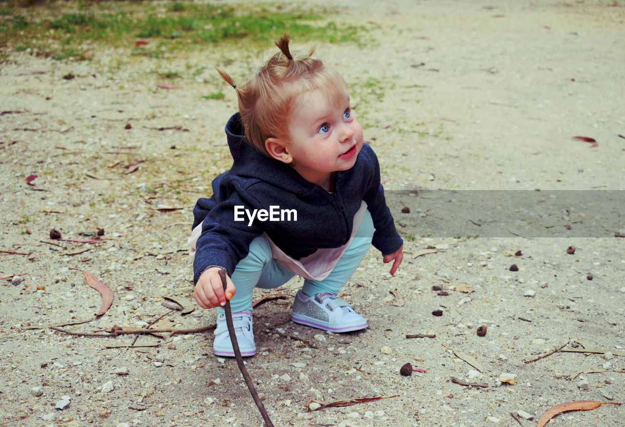 Baby girl holding stick while looking away against trees on field