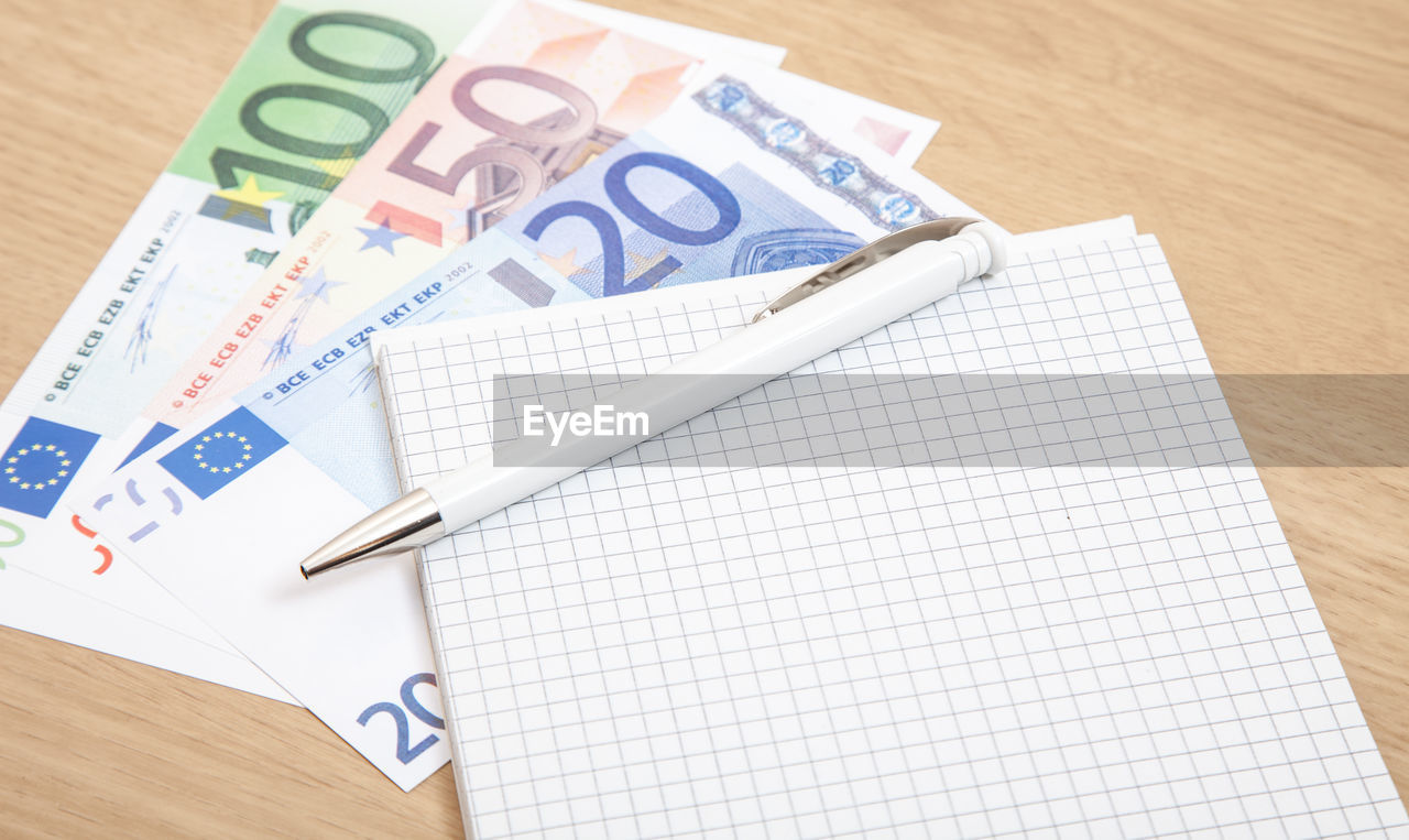 High angle view of pen and book euro banknotes on table