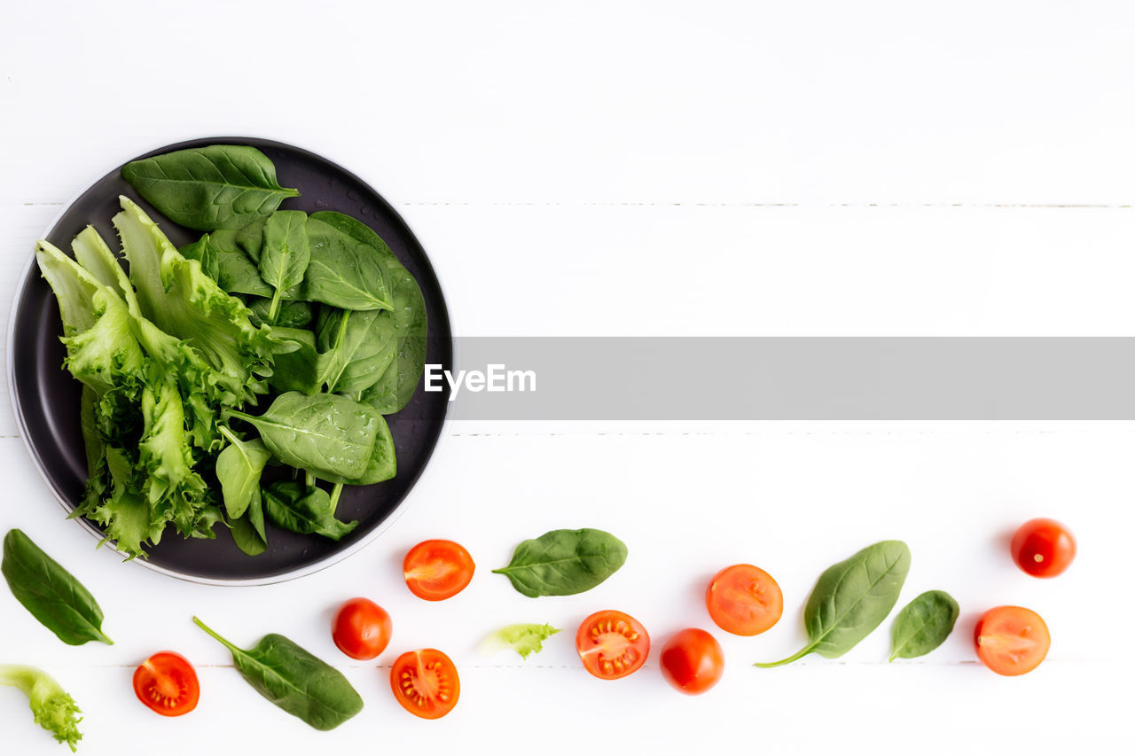 Bowl of fresh salad leaves, lettuce, spinach and red cherry tomatoes and halves on white background