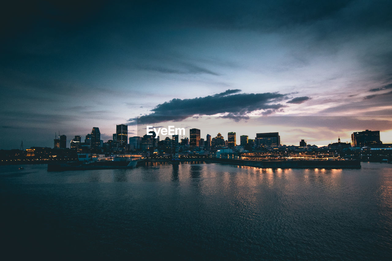 Scenic view of river by buildings against sky at dusk