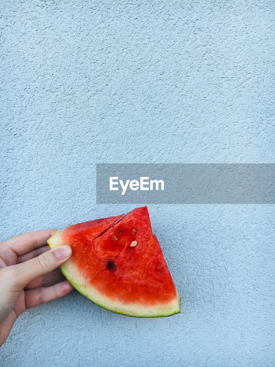 Cropped image of hand holding watermelon against wall