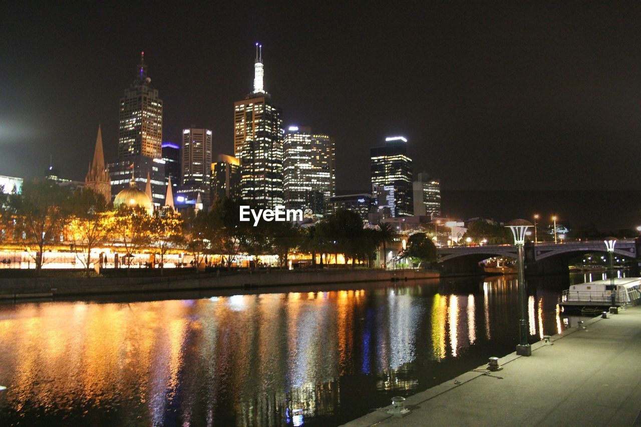 Illuminated city by river at night