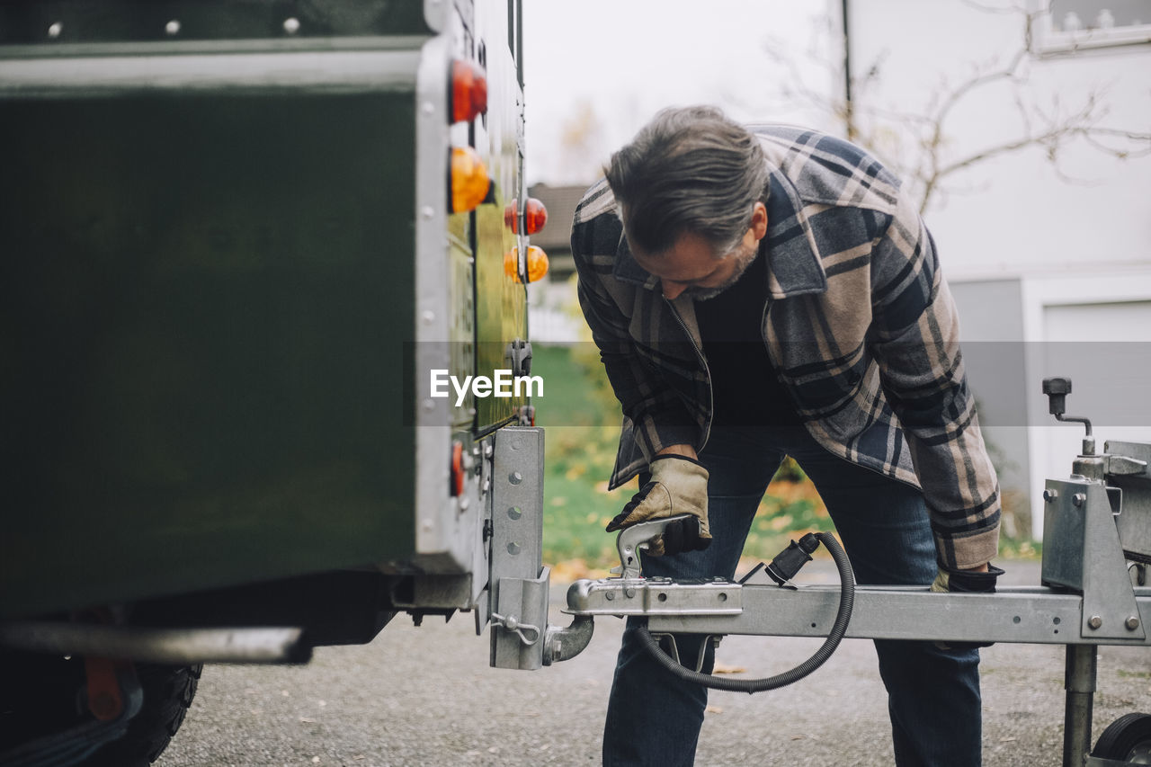 Mature man towing trailer to sports utility vehicle on driveway