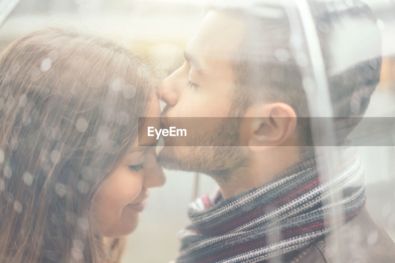 Close-up of man kissing on woman forehead seen through umbrella