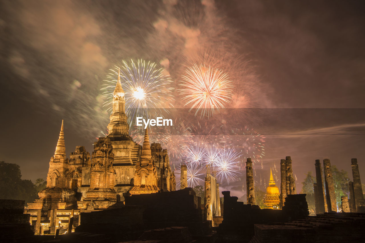 FIREWORK DISPLAY OVER ILLUMINATED BUILDING AGAINST SKY