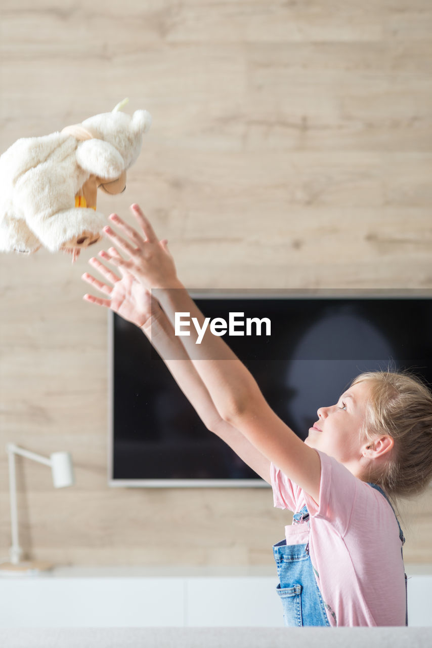 Side view of girl playing with teddy bear at home