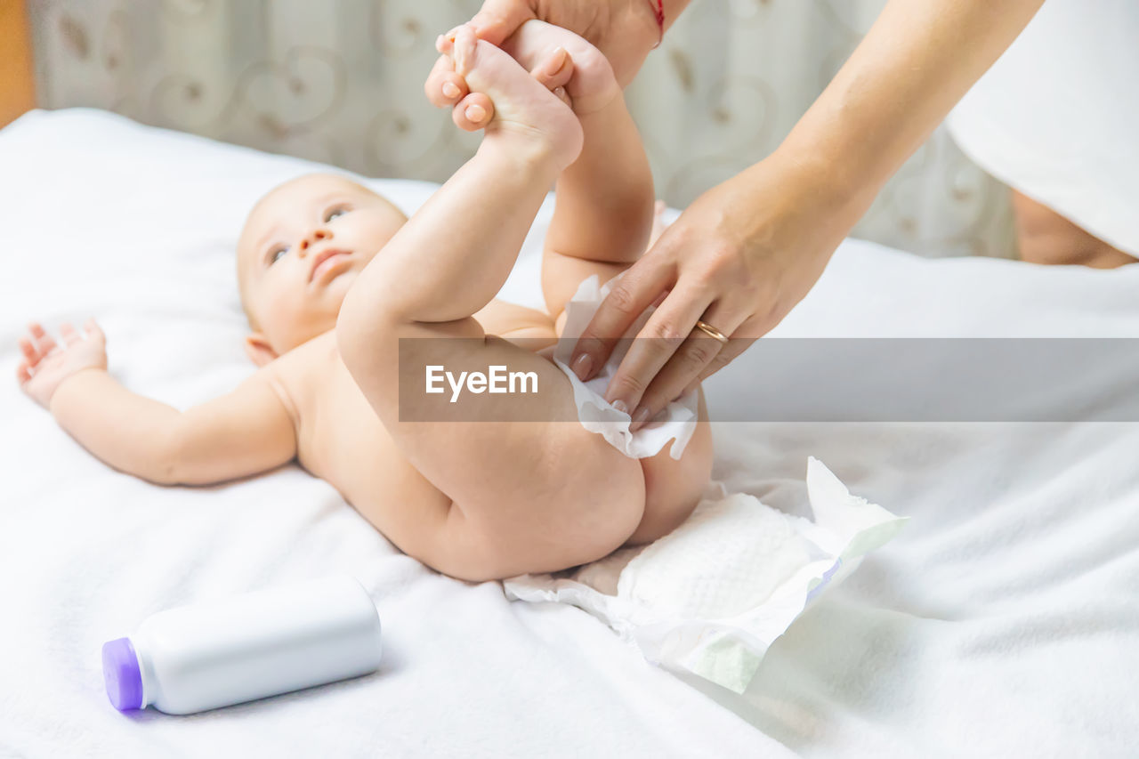 Mother cleaning baby lying on bed at home