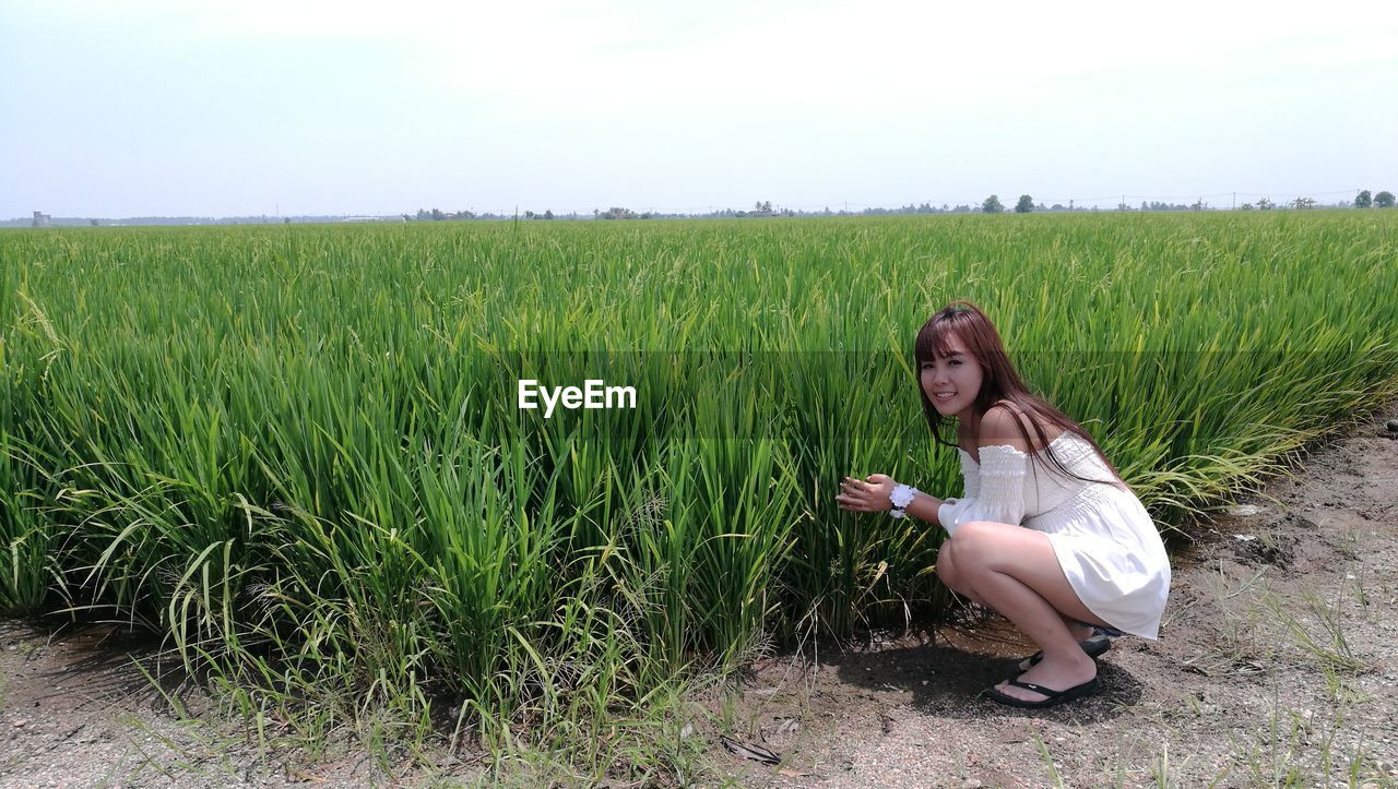 Woman crouching by crop on field