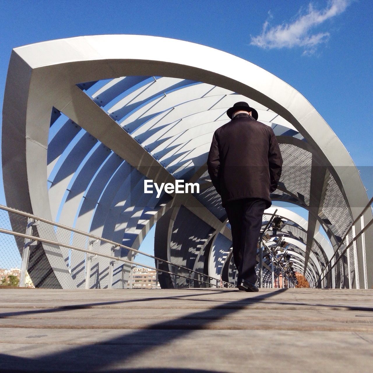 Full length rear view of man walking on modern footbridge against sky