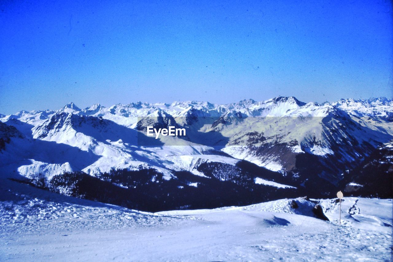 snow, winter, cold temperature, mountain, scenics - nature, beauty in nature, mountain range, snowcapped mountain, environment, sky, landscape, nature, tranquil scene, blue, tranquility, no people, clear sky, day, non-urban scene, outdoors, piste, white, travel destinations, travel, winter sports, sports, frozen