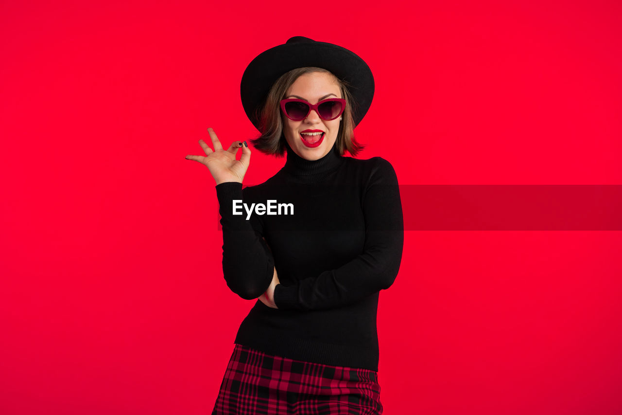 PORTRAIT OF YOUNG WOMAN WEARING SUNGLASSES AGAINST RED BACKGROUND