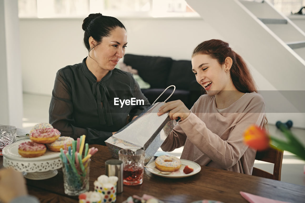 Smiling mother looking at excited daughter with gift during birthday party