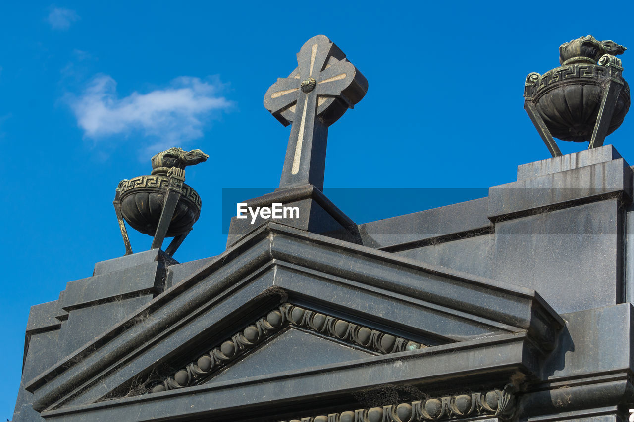 Low angle view of cross on statue against blue sky