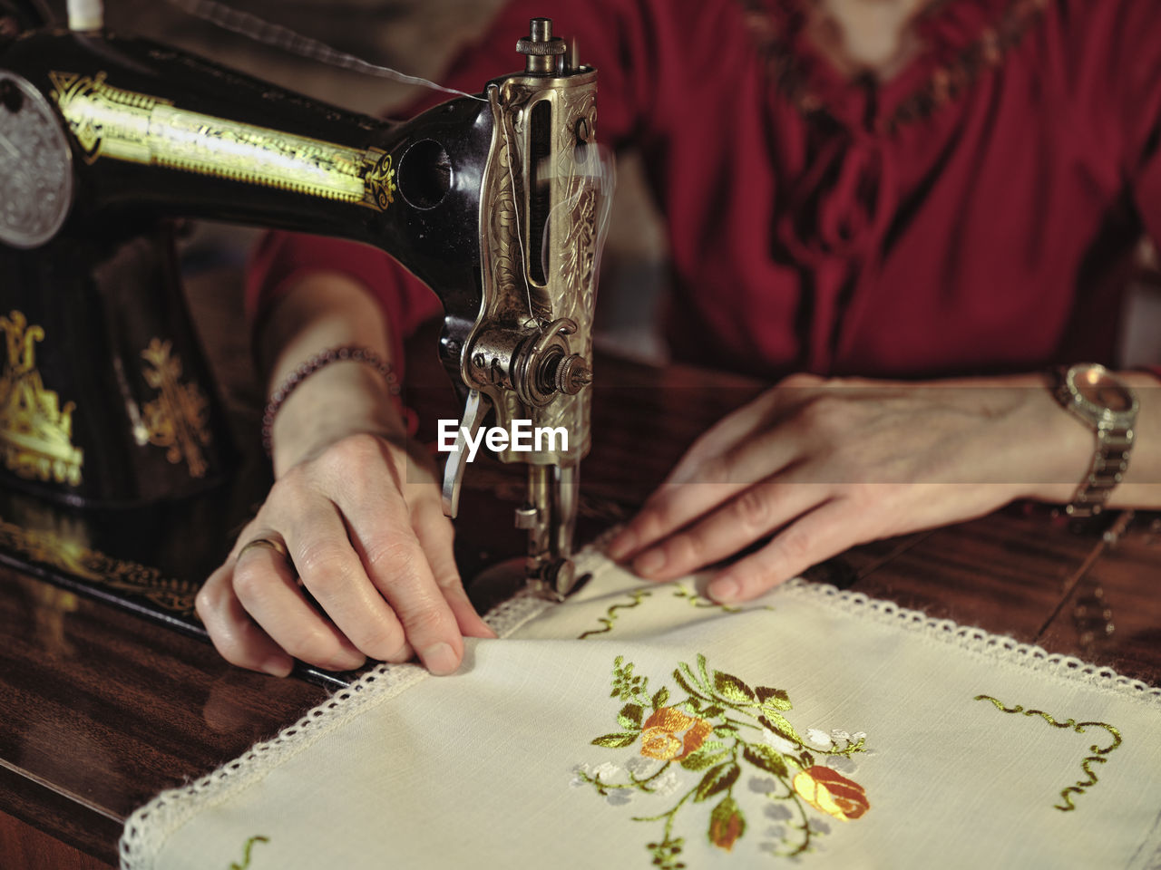 Senior lady in glasses using retro sewing machine to create linen napkin in cozy room at home